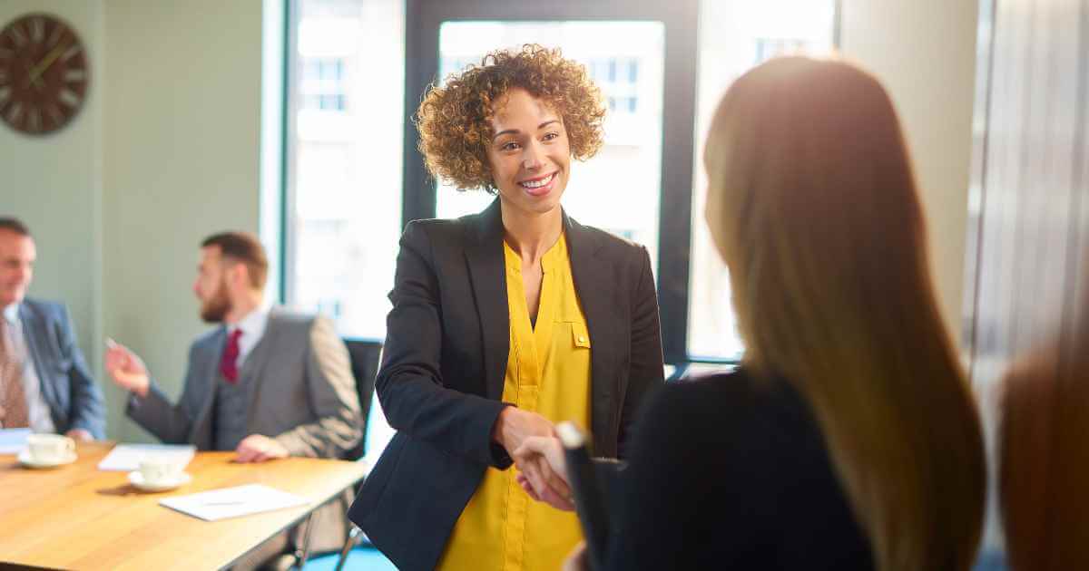 Woman in a yellow dress suit shaking the hand of a job candidate