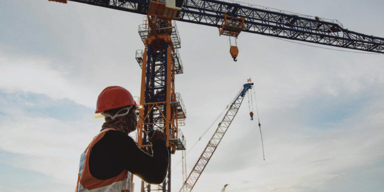 Construction worker with back to camera looks up at cranes overhead.